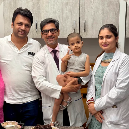 Dr. Sumit Mrig holding a young patient, with the child's father and a colleague at the clinic